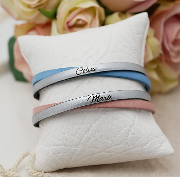 Bracelets personnalisés en cuir avec prénoms gravés sur coussin.