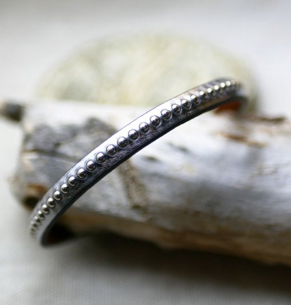 Damearmb&aring;nd i m&oslash;rkegr&aring;t metallisk l&aelig;der med s&oslash;lvfarvede perler 