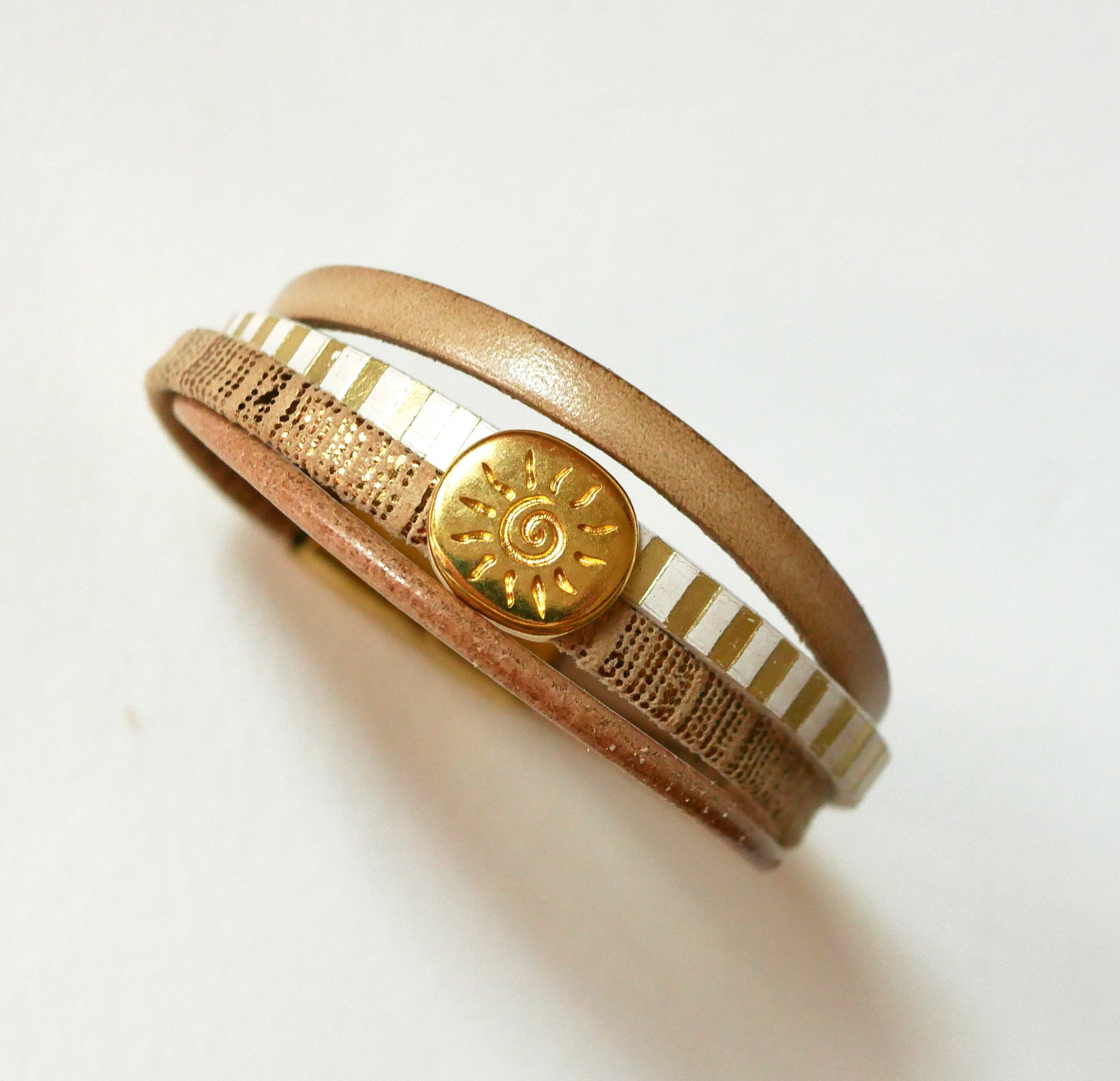 Manchetarmb&aring;nd i l&aelig;der med flere led og guldfarvet solstr&aring;lesl&oslash;jfe