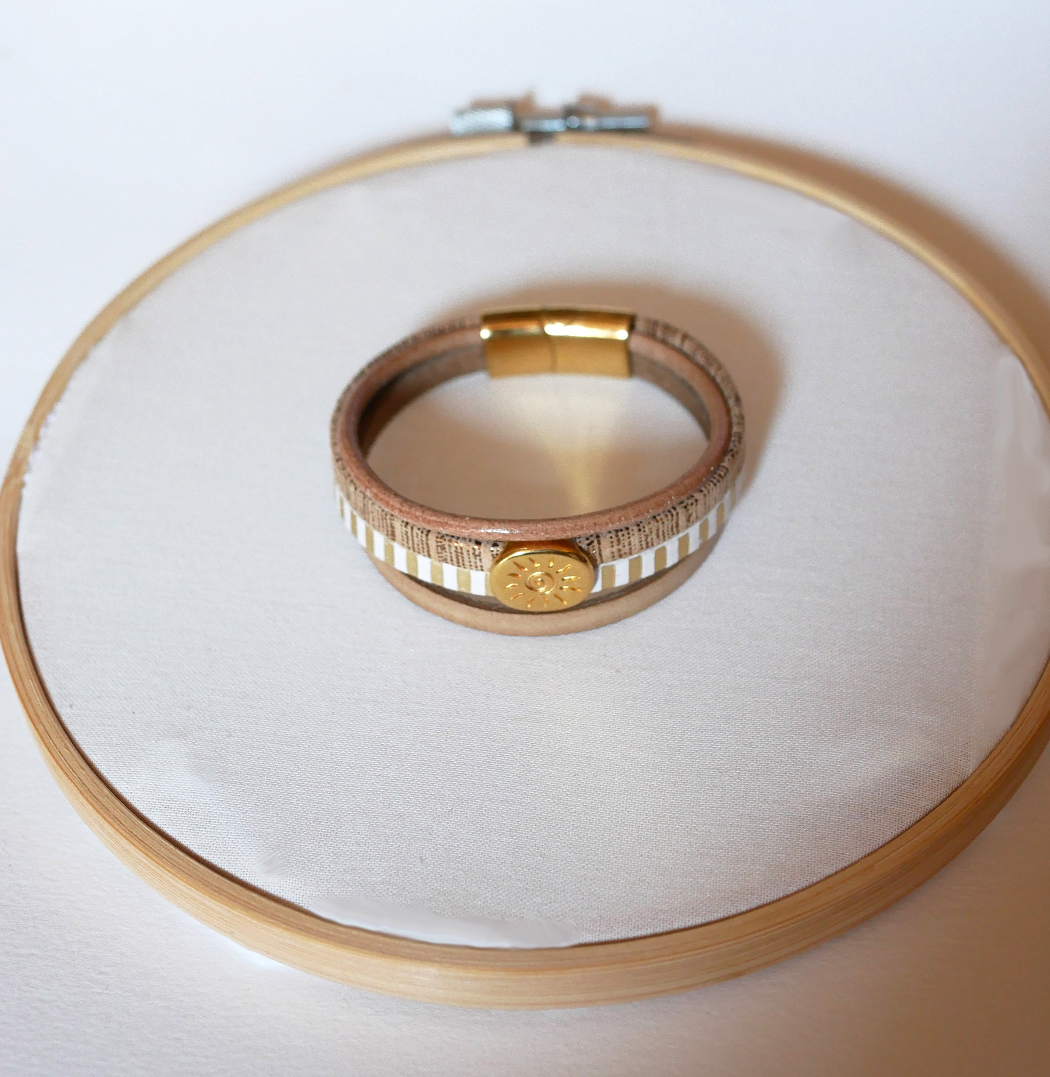 Manchetarmb&aring;nd i l&aelig;der med flere led og guldfarvet solstr&aring;lesl&oslash;jfe