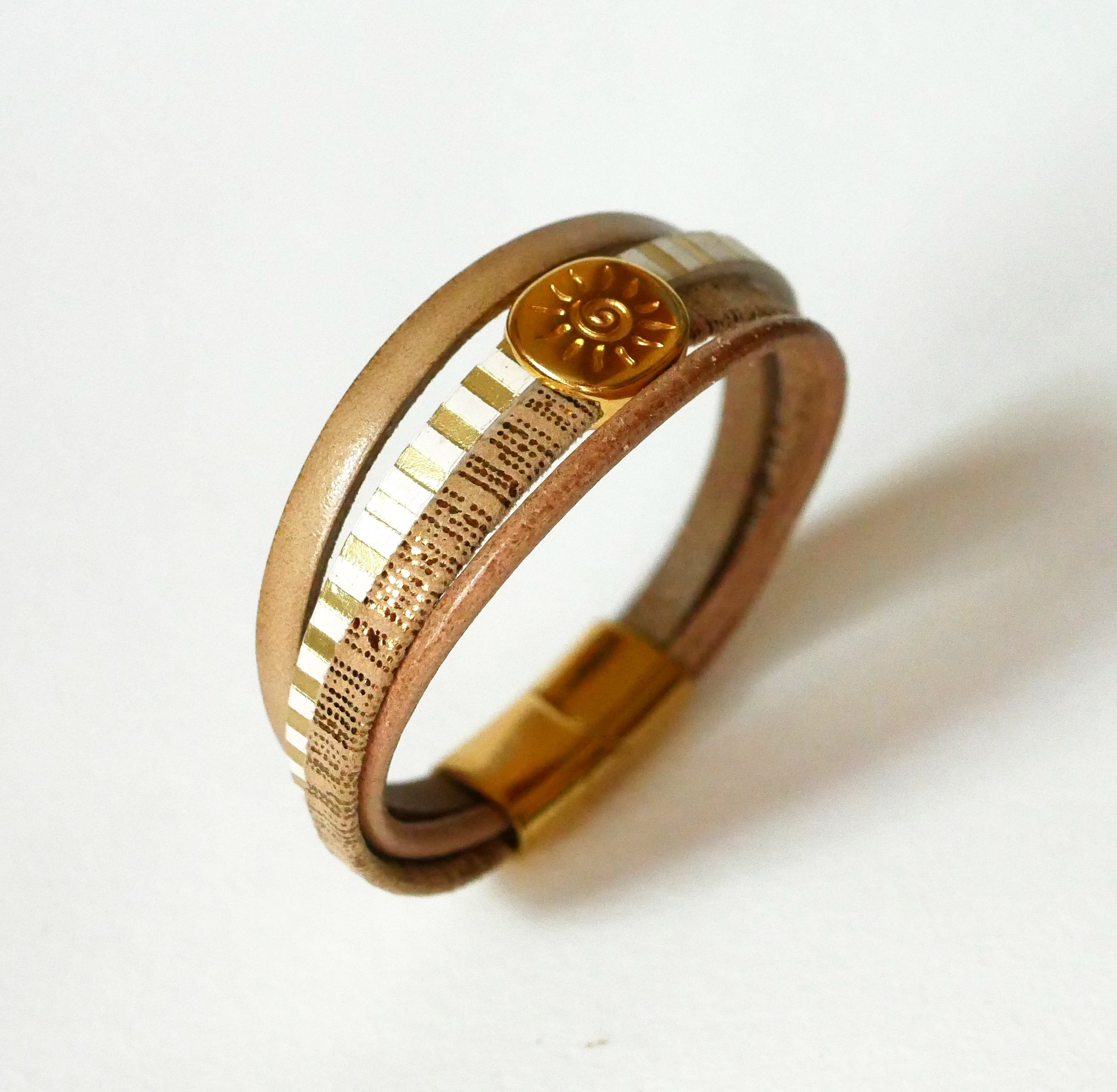 Manchetarmb&aring;nd i l&aelig;der med flere led og guldfarvet solstr&aring;lesl&oslash;jfe