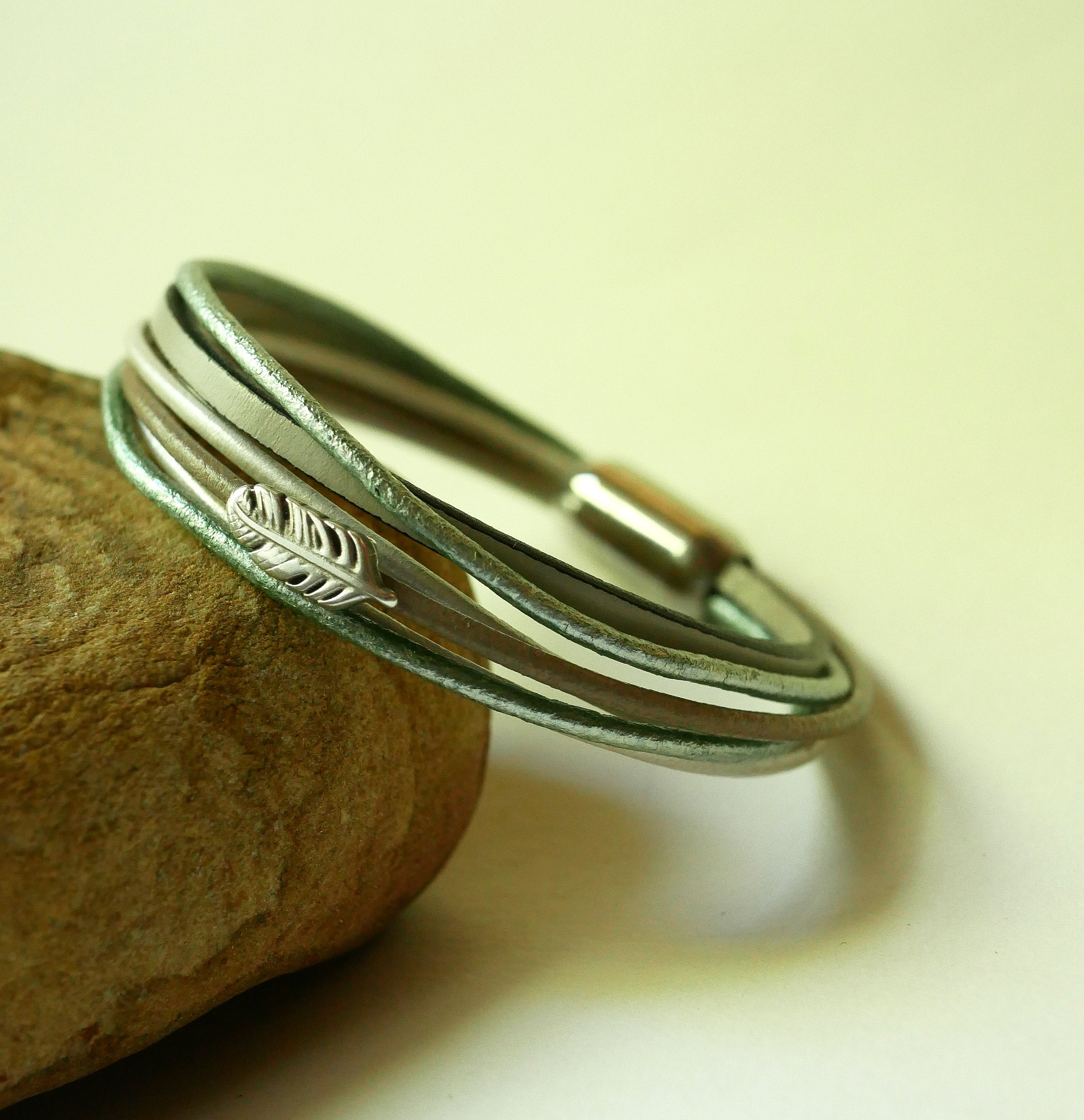 Multi-l&aelig;derarmb&aring;nd i nuancer af beige, lysegr&oslash;n og perlemor, dekoreret med en lille fjer