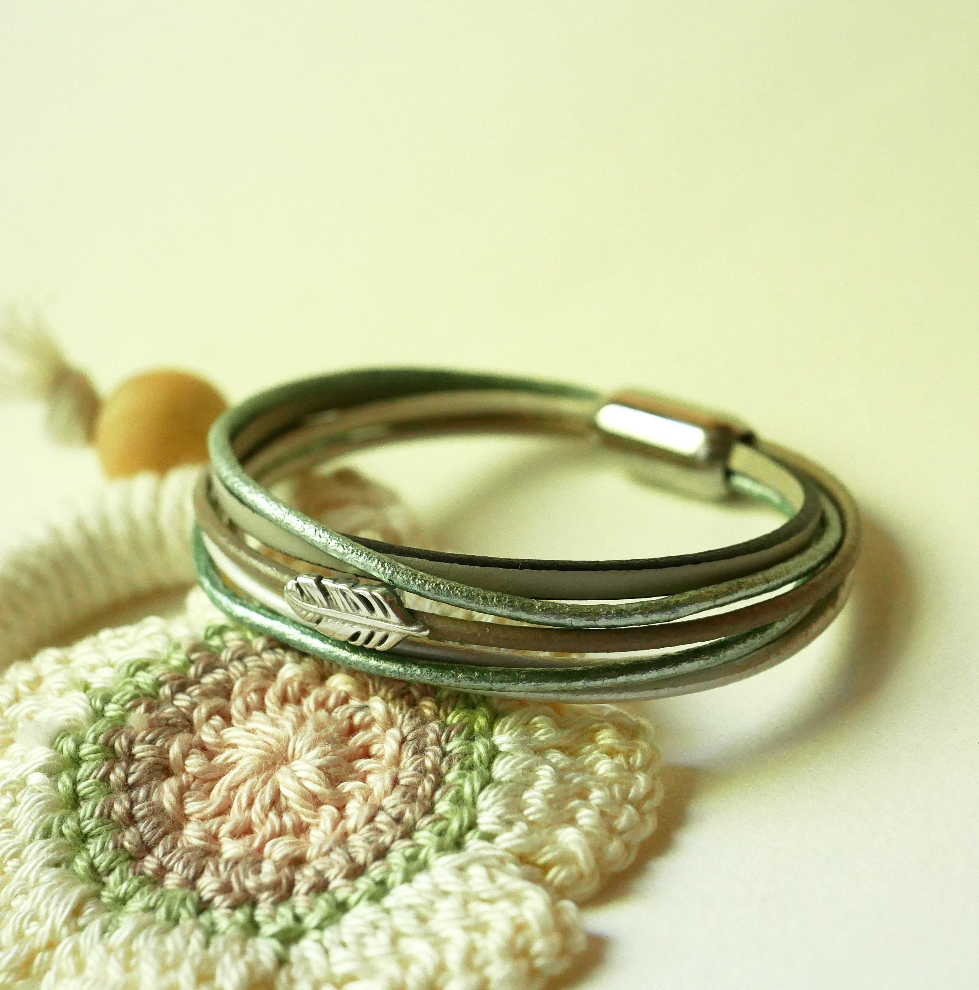 Multi-læderarmbånd i nuancer af beige, lysegrøn og perlemor, dekoreret med en lille fjer