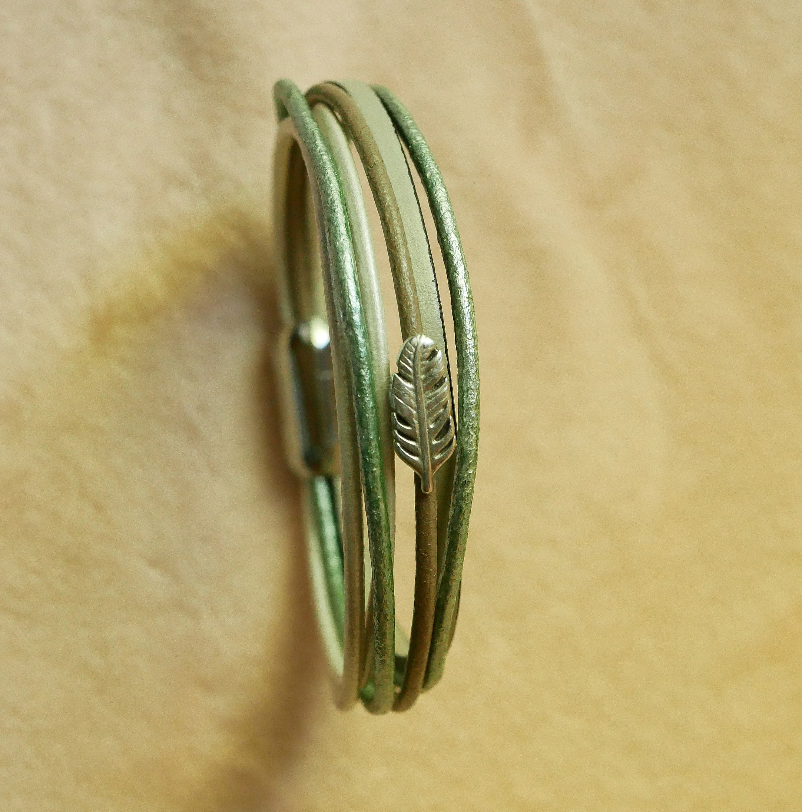 Multi-l&aelig;derarmb&aring;nd i nuancer af beige, lysegr&oslash;n og perlemor, dekoreret med en lille fjer