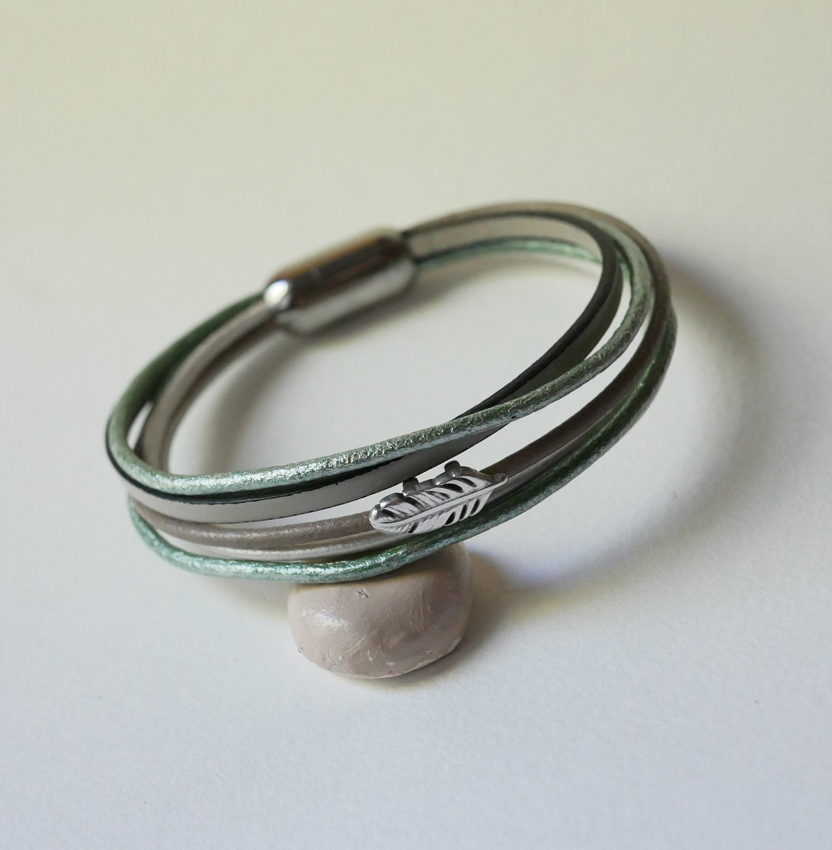 Multi-læderarmbånd i nuancer af beige, lysegrøn og perlemor, dekoreret med en lille fjer