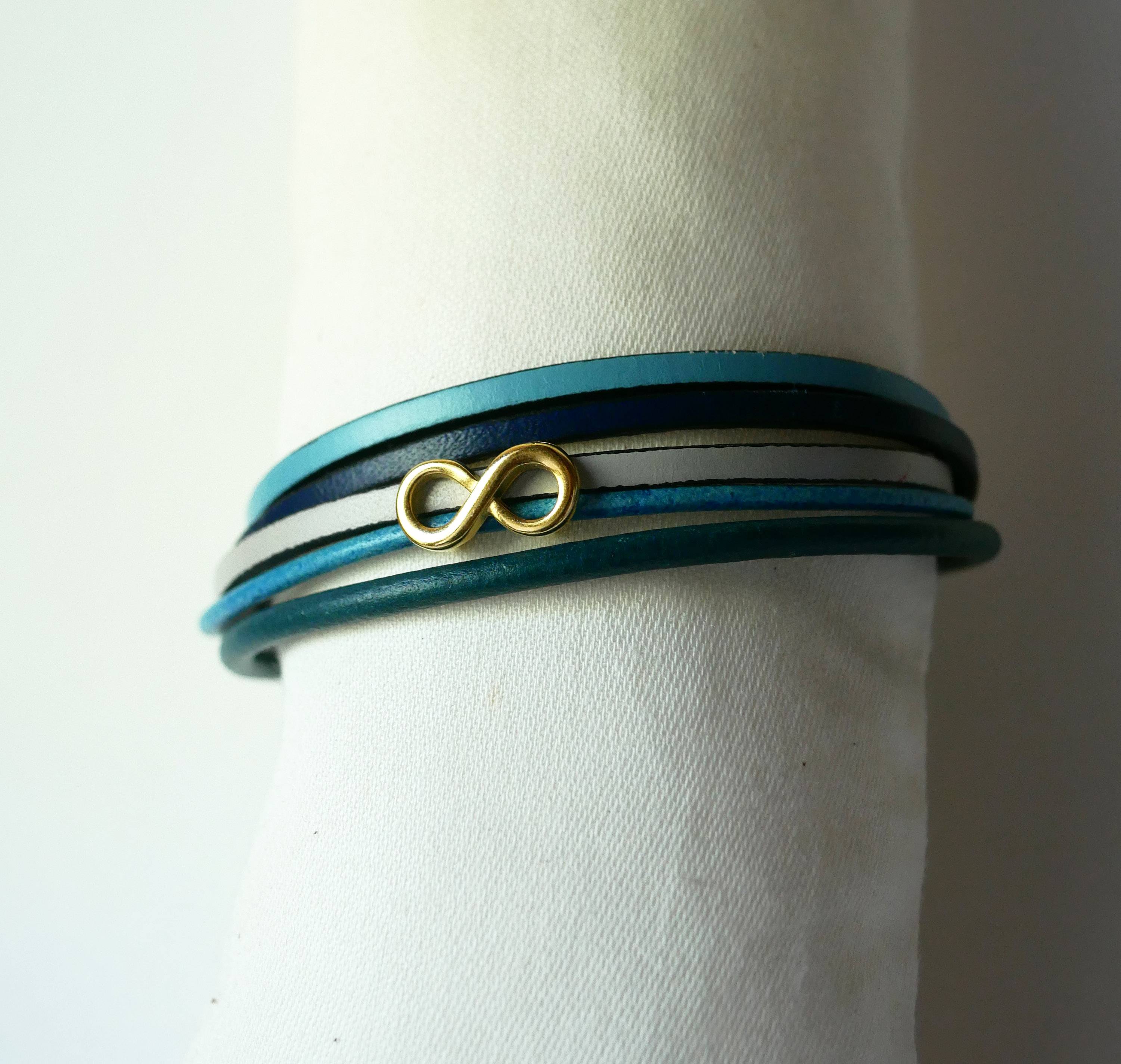 Flerleddet armbånd i blåtonet læder med infinity-motiv i guld