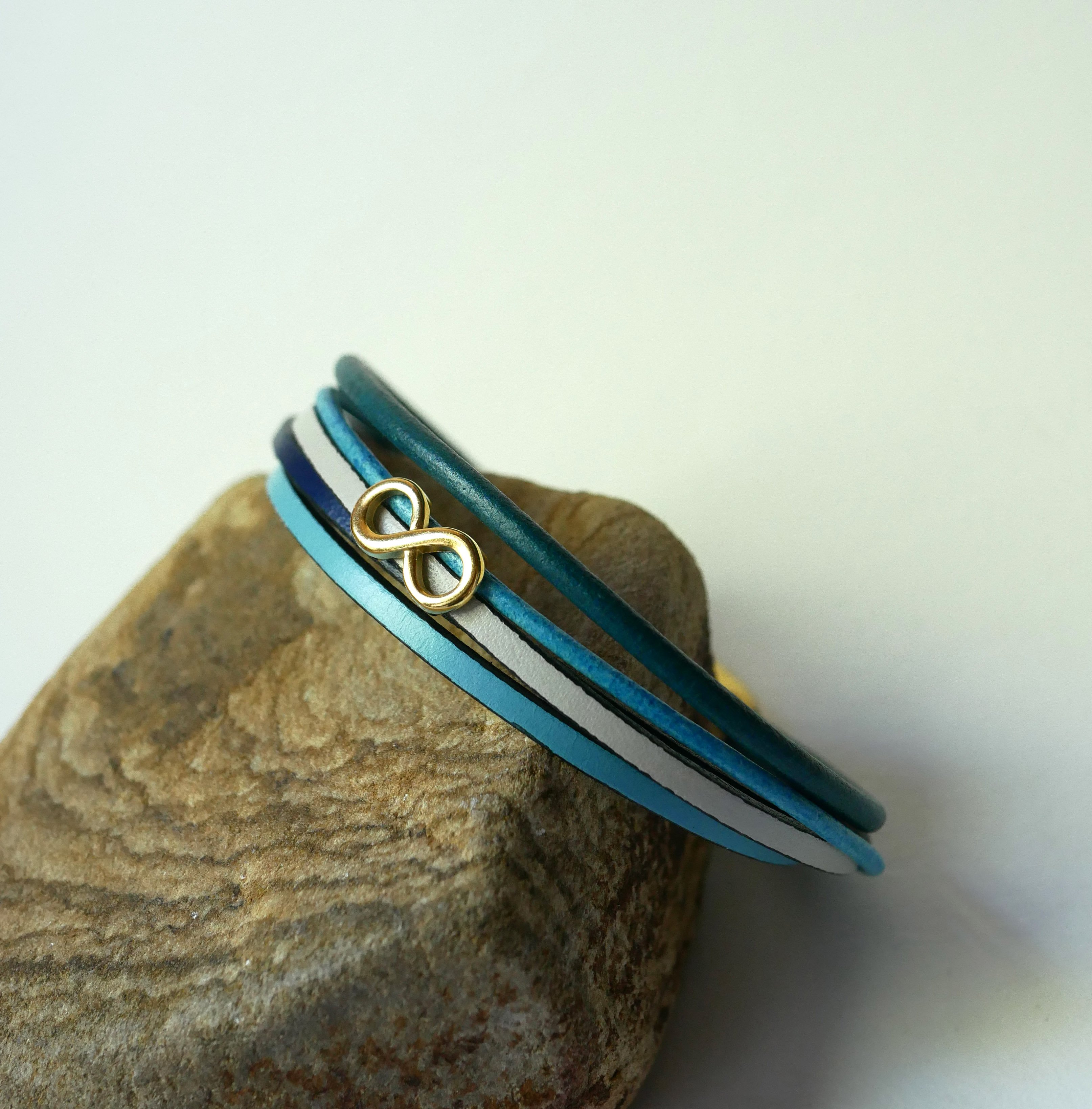 Flerleddet armbånd i blåtonet læder med infinity-motiv i guld
