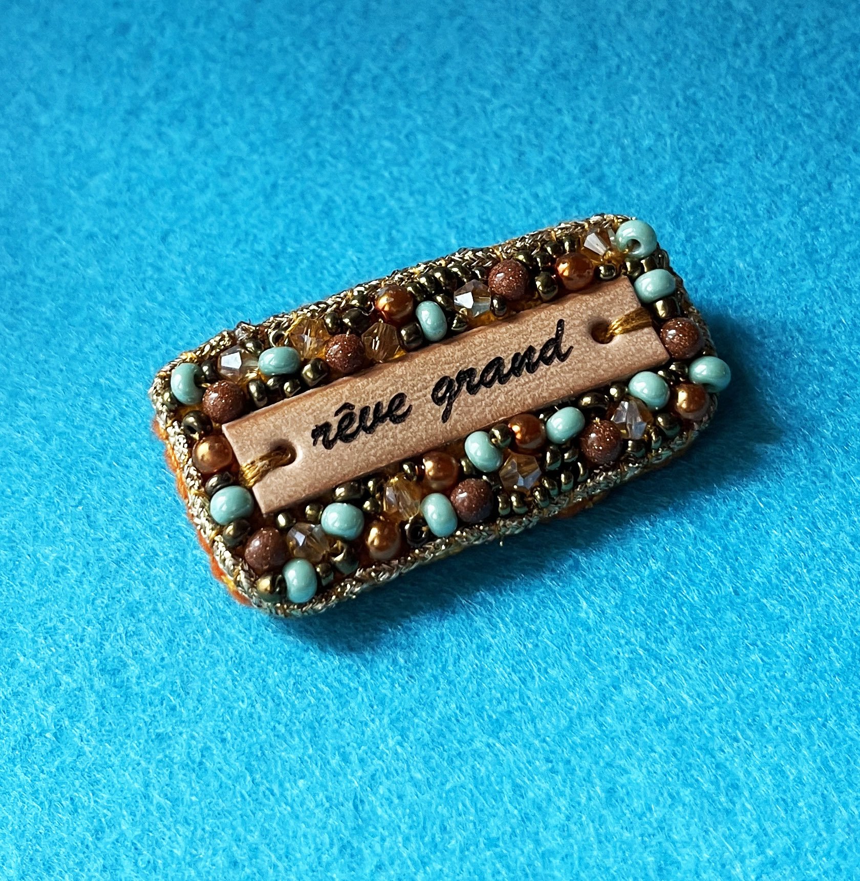 Broche en perles dor&eacute;es &agrave; message en cuir grav&eacute; "r&ecirc;ve grand"