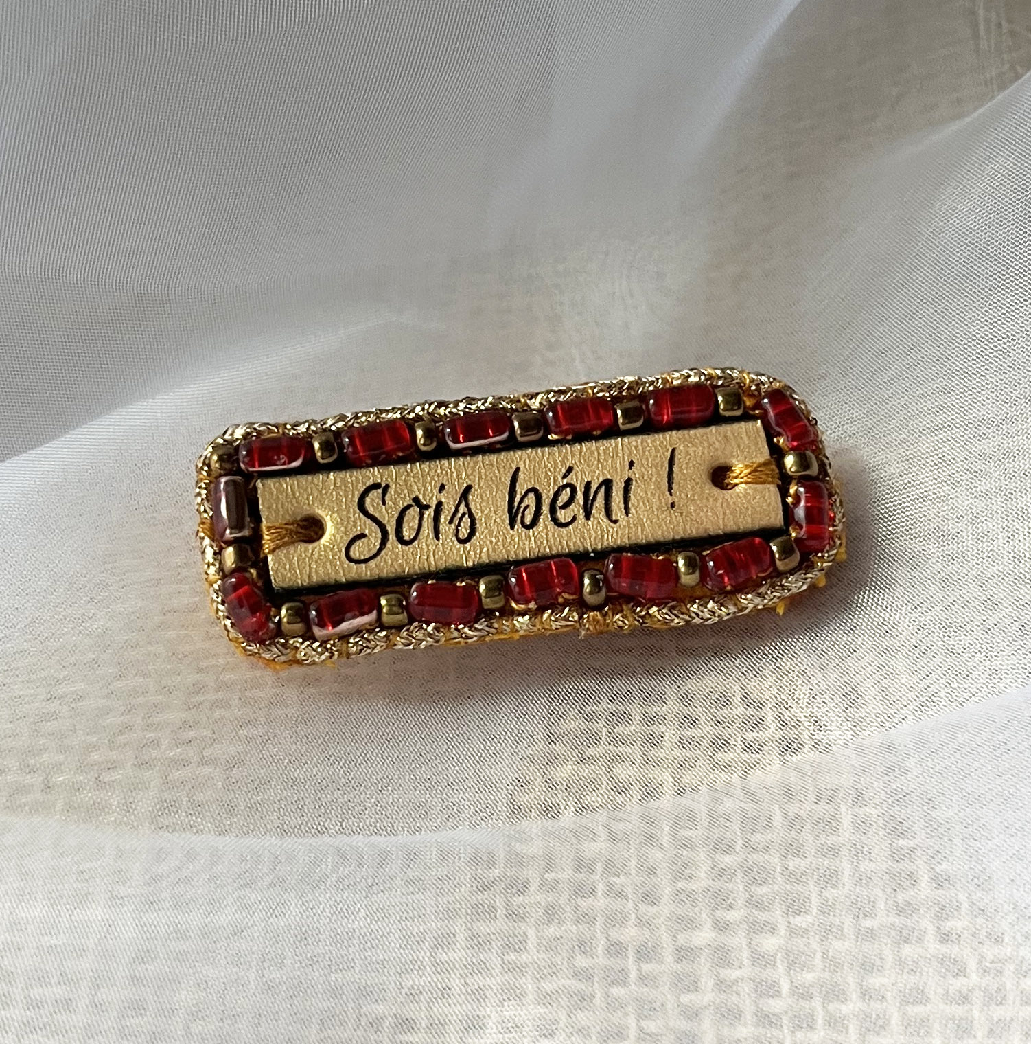 Broche à message en cuir gravé "sois béni" en perles rouges et dorées 