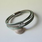 Multi-læderarmbånd i nuancer af beige, lysegrøn og perlemor, dekoreret med en lille fjer